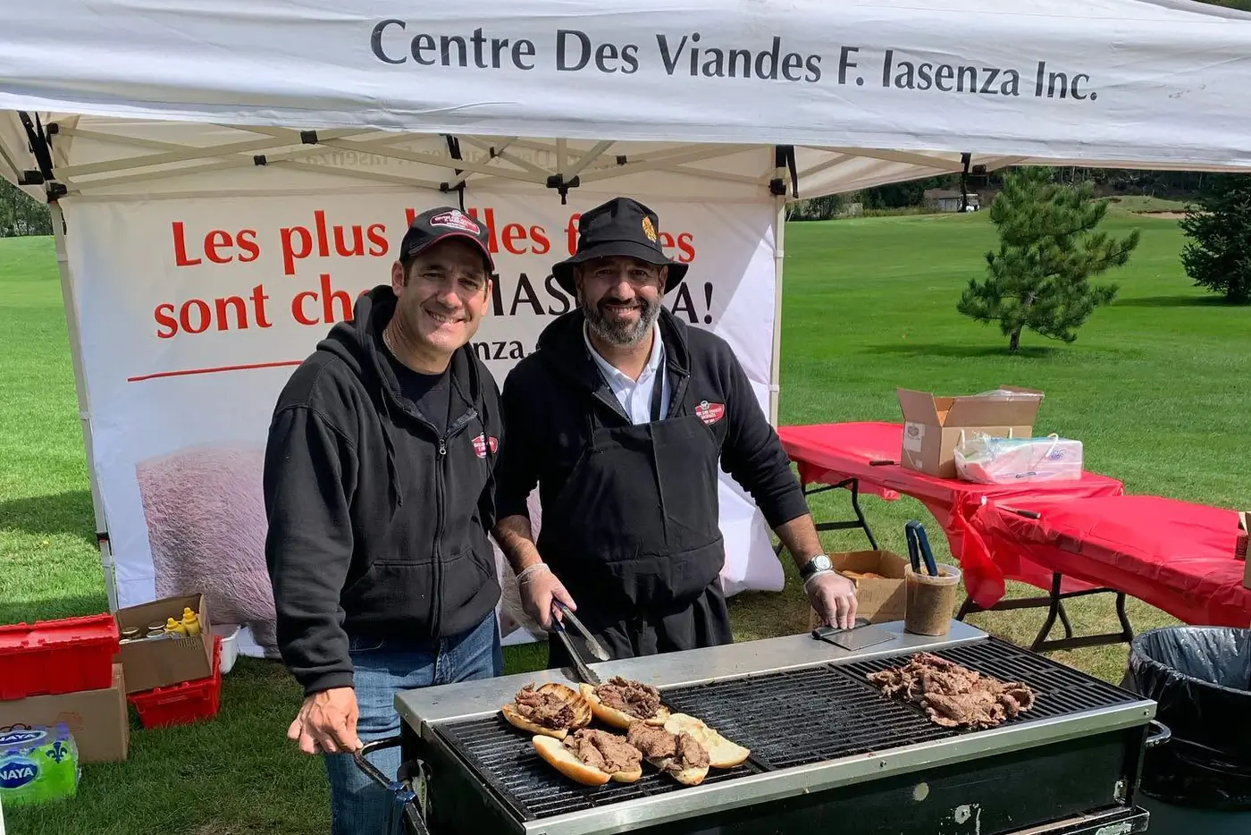 Deux membres de l'équipe Iasenza font griller des sandwichs à la viande sous une tente Centre des Viandes F. Iasenza, lors d'un événement extérieur