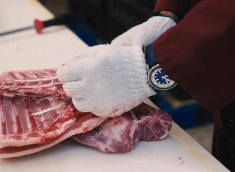 Un boucher Iasenza, gants de coupe aux mains, pare une pièce de viande au comptoir