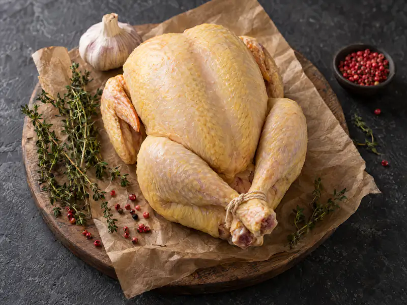 Poulet entier cru nourri au grain, ficelé, sur une planche de bois
